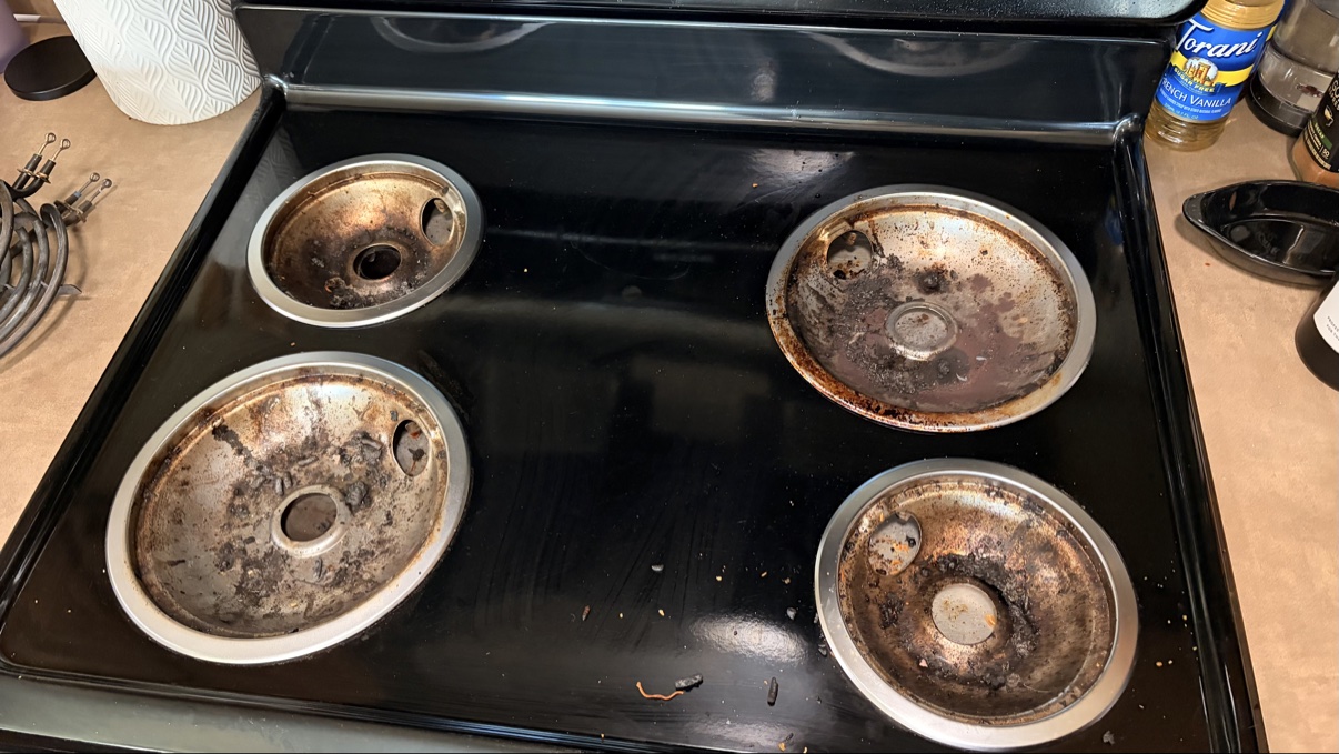 Burnt, grease-covered stovetop drip pans before cleaning